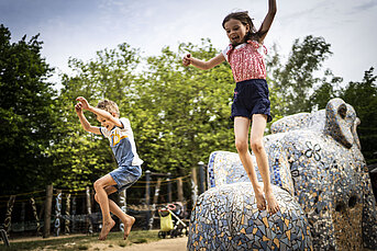 Kinder springen von Elefanten am Lehmdorf-Spielplatz im Britzer Garten
