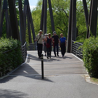 Personen laufen bei Sonnenschein über die Rhizomatische Brücke